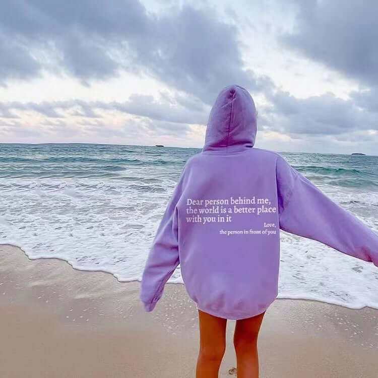Dear Person Behind Me the World Is A Better Place with You hoodie worn on the beach with ocean backdrop.