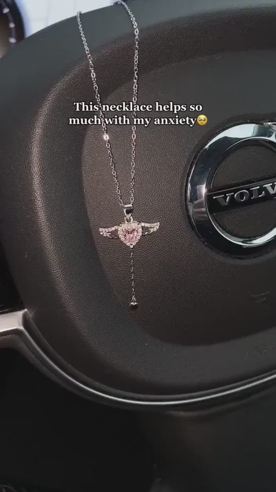 Moving Cupid Heart Angel Wings Tassel Necklace With Crystal displayed on a car steering wheel.
